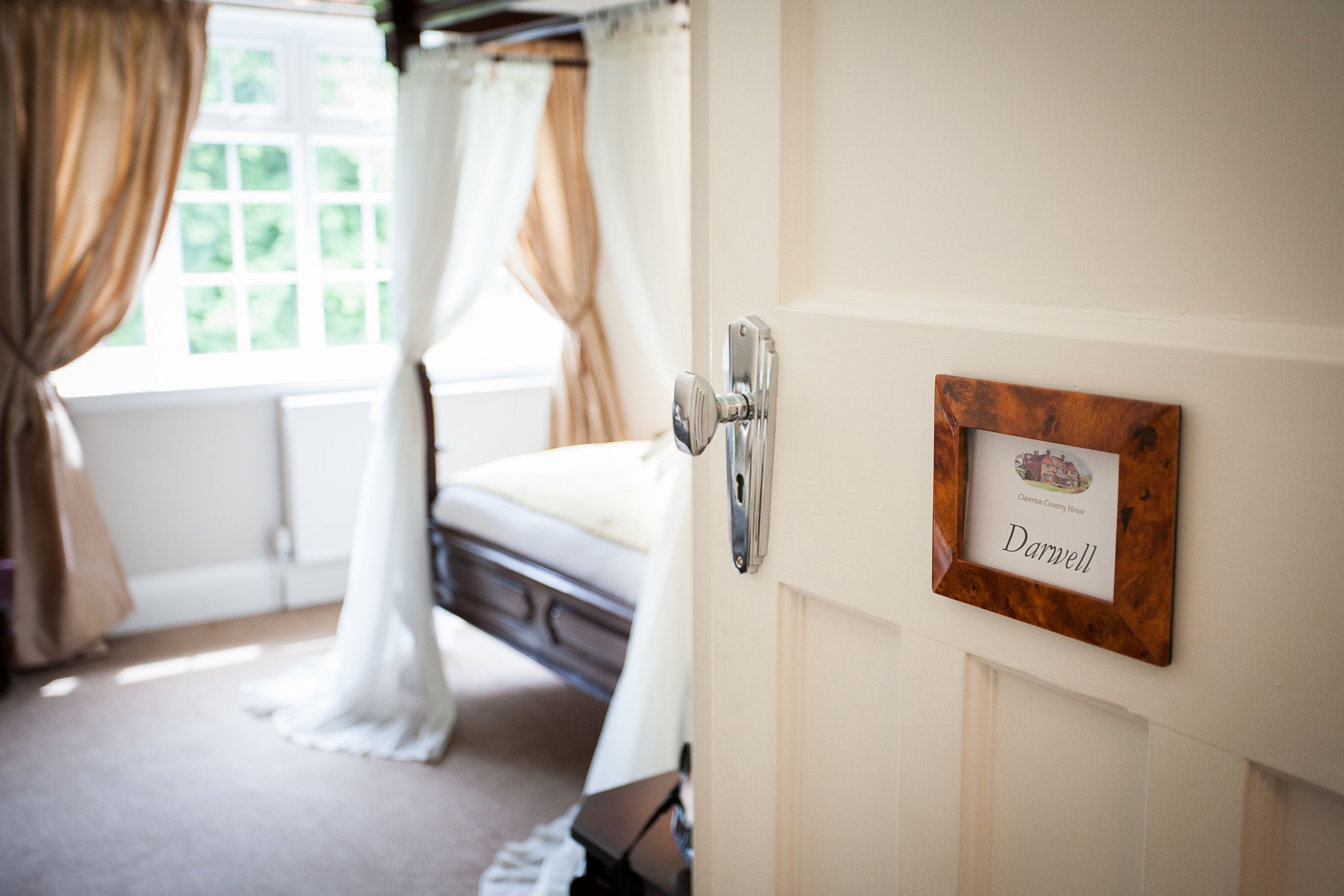A bedroom with a bed, a door with a nameplate, and a window with curtains.