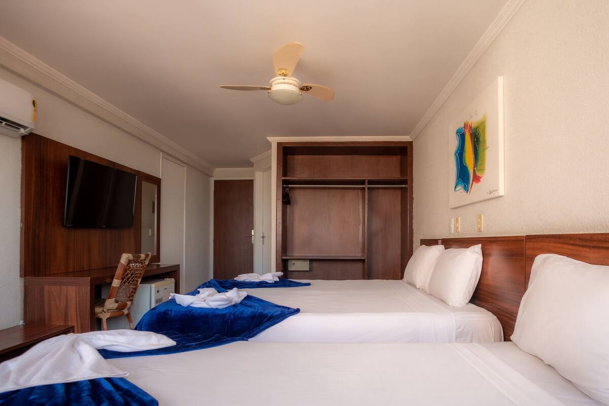 Ein Hotelzimmer mit zwei Betten, einem Deckenventilator, einem Fernseher, einem Kleiderschrank und einem Bild an der Wand.