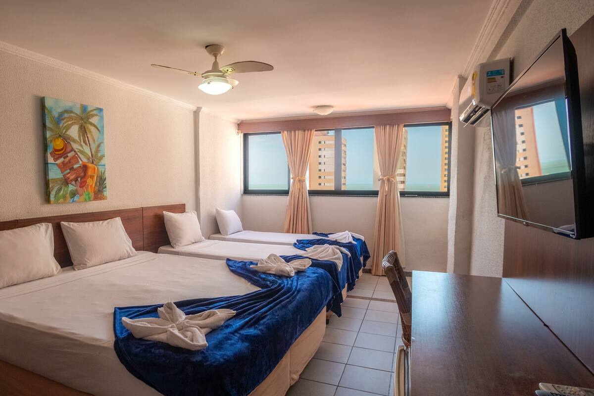 Ein Hotelzimmer mit zwei Betten, einem Deckenventilator, einem Gemälde, einem Fernseher und einem Fenster mit Vorhängen.