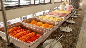 Buffet com diversos alimentos, incluindo fatias de laranja, fruta amarela e carne rosa.