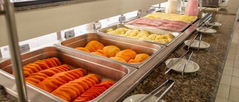 A buffet with various food items including orange slices, yellow fruit, and pink meat.
