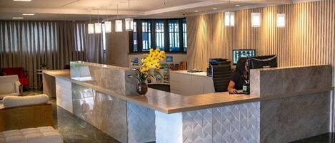 Ett receptionsområde med en marmorskiva, en receptionist och ett stort fönster med gardiner.
