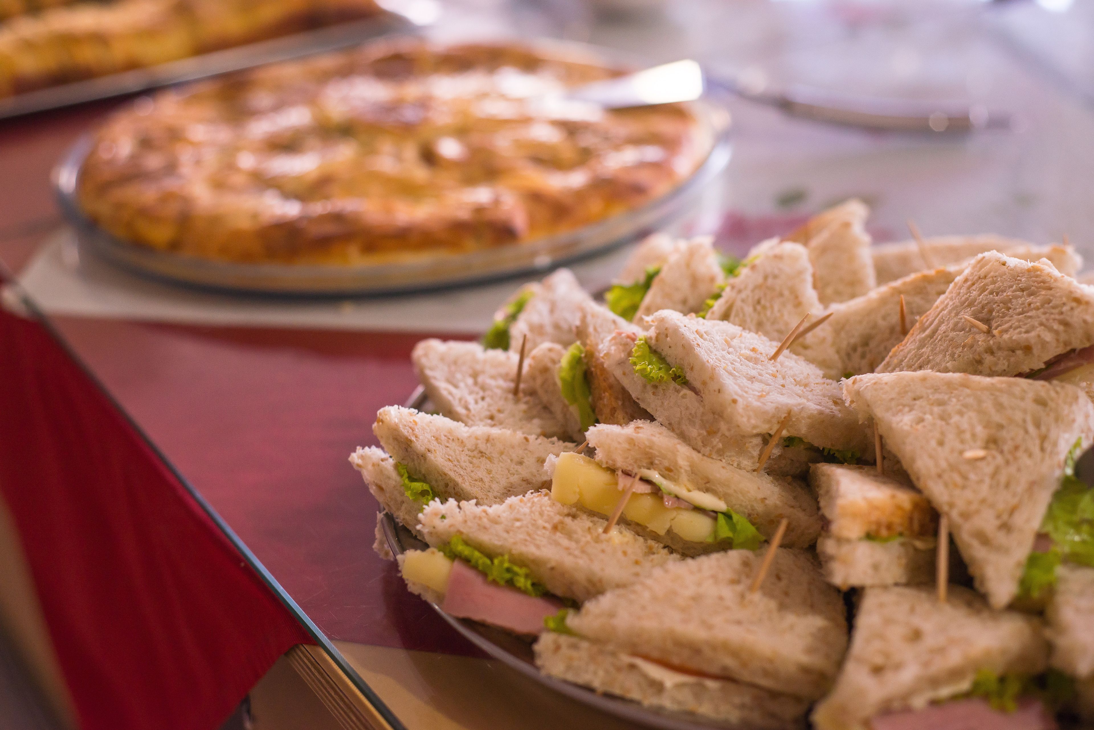 A plate of sandwiches and a pizza on a table.