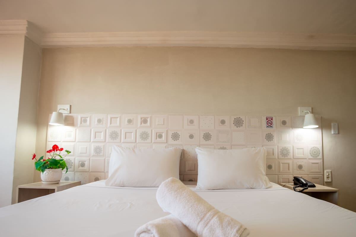Ein Hotelzimmer mit einem großen Bett, zwei Nachttischlampen, einer Zimmerpflanze und einem Telefon auf dem Nachttisch.