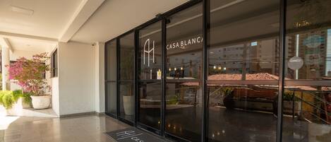 A hotel entrance with a glass facade, a potted plant, and a doormat with the hotel's name.