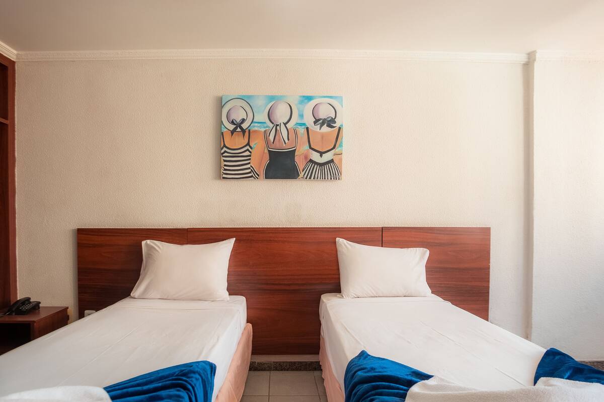 Ein Hotelzimmer mit zwei Betten, einem Holzkopfstück, einem Bild an der Wand und einem Telefon auf einem Nachttisch.
