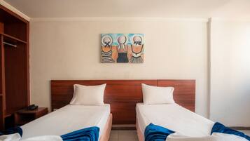 Quarto de hotel com duas camas, cabeceira de madeira, um quadro na parede e um telefone em uma mesinha de cabeceira.