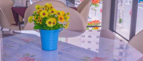 A table with a floral tablecloth, a blue vase with yellow flowers, and beige chairs.