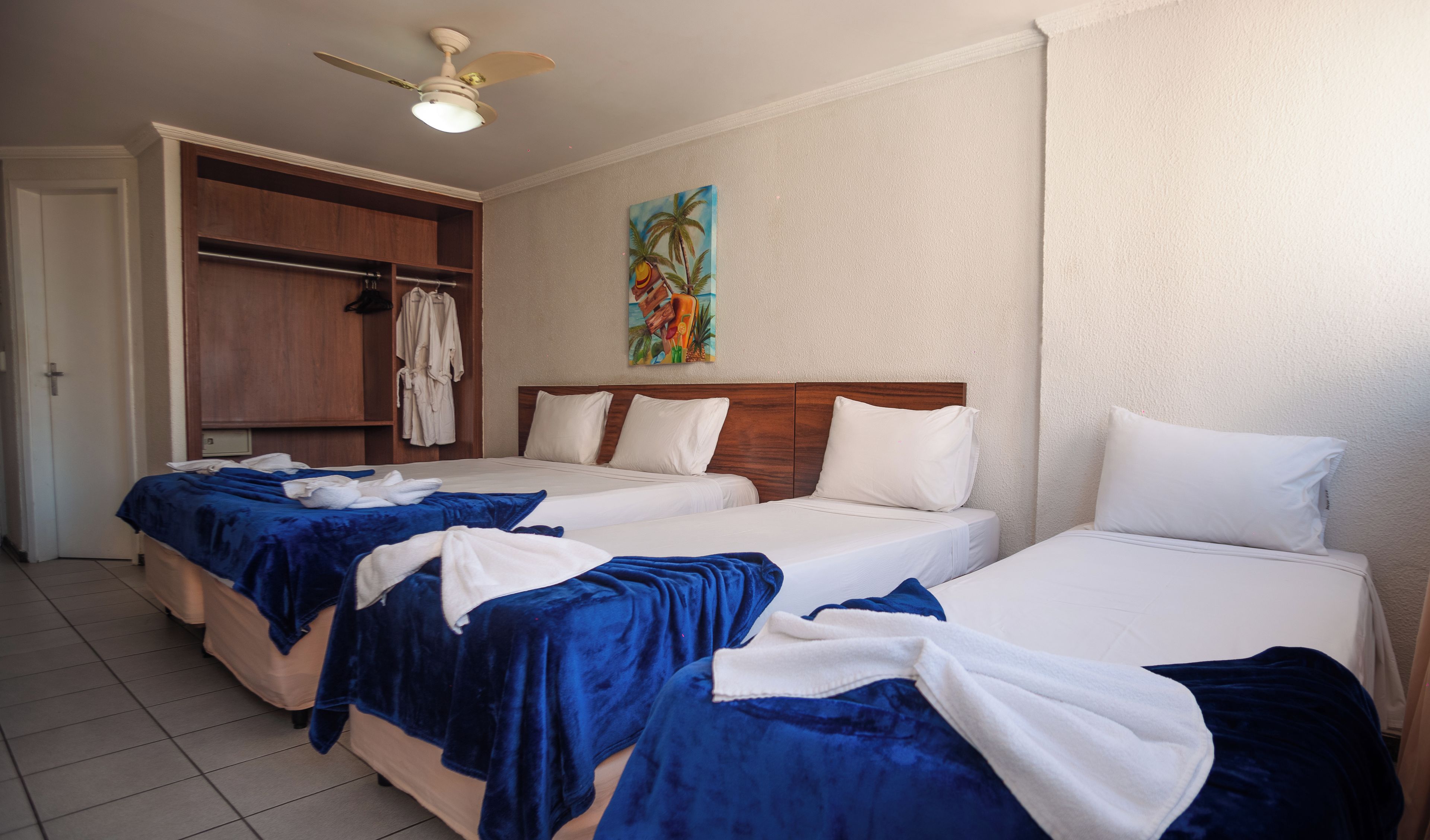 Quarto de hotel com duas camas, um guarda-roupa de madeira e um ventilador de teto.