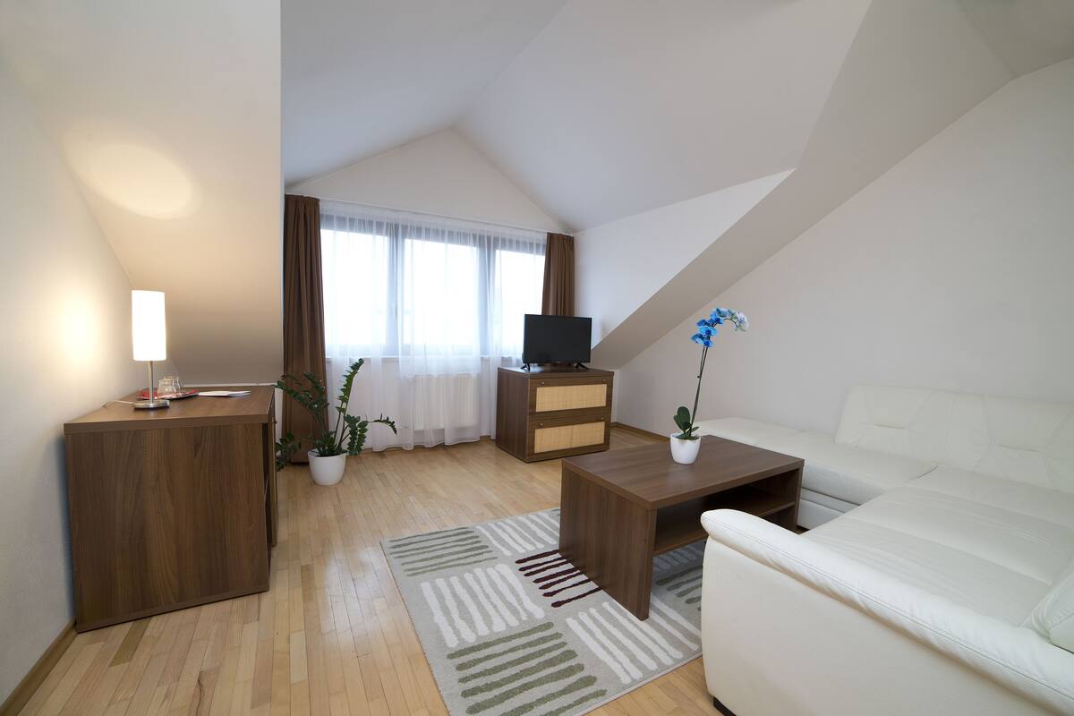 A modern living room with a wooden desk, a white sofa, a TV stand, and a potted plant.