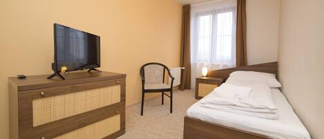 Habitación de hotel con una cama, un televisor en una cómoda, una silla y una mesita de noche con lámpara.