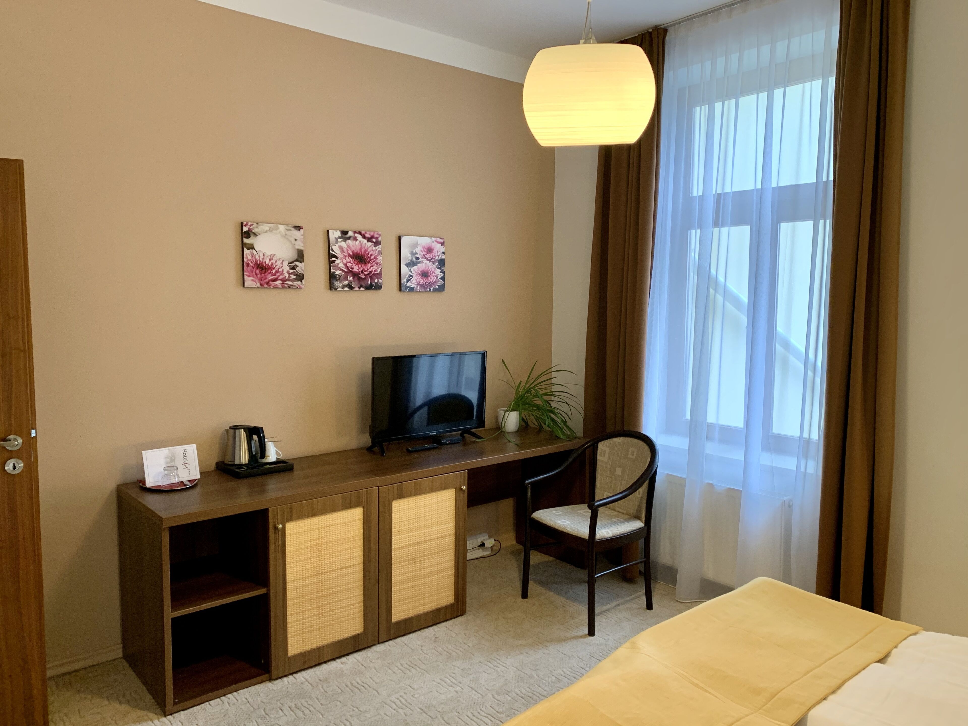 A hotel room with a wooden desk, a television, a chair, and a bed.