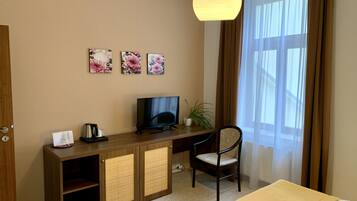 A hotel room with a wooden desk, a television, a chair, and a bed.