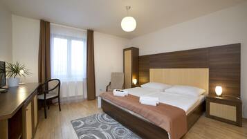 Een hotelkamer met een bed, nachtkastje, bureau, stoel en een potplant.