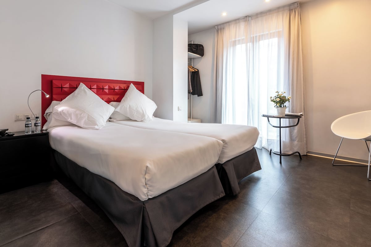 A hotel room with a large bed, a bedside table with a lamp, a small table with a plant, and a chair.