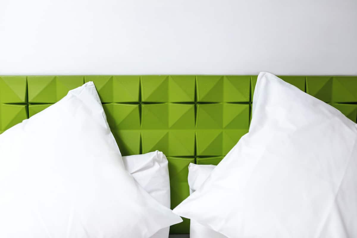 A bed with a green headboard and white pillows.