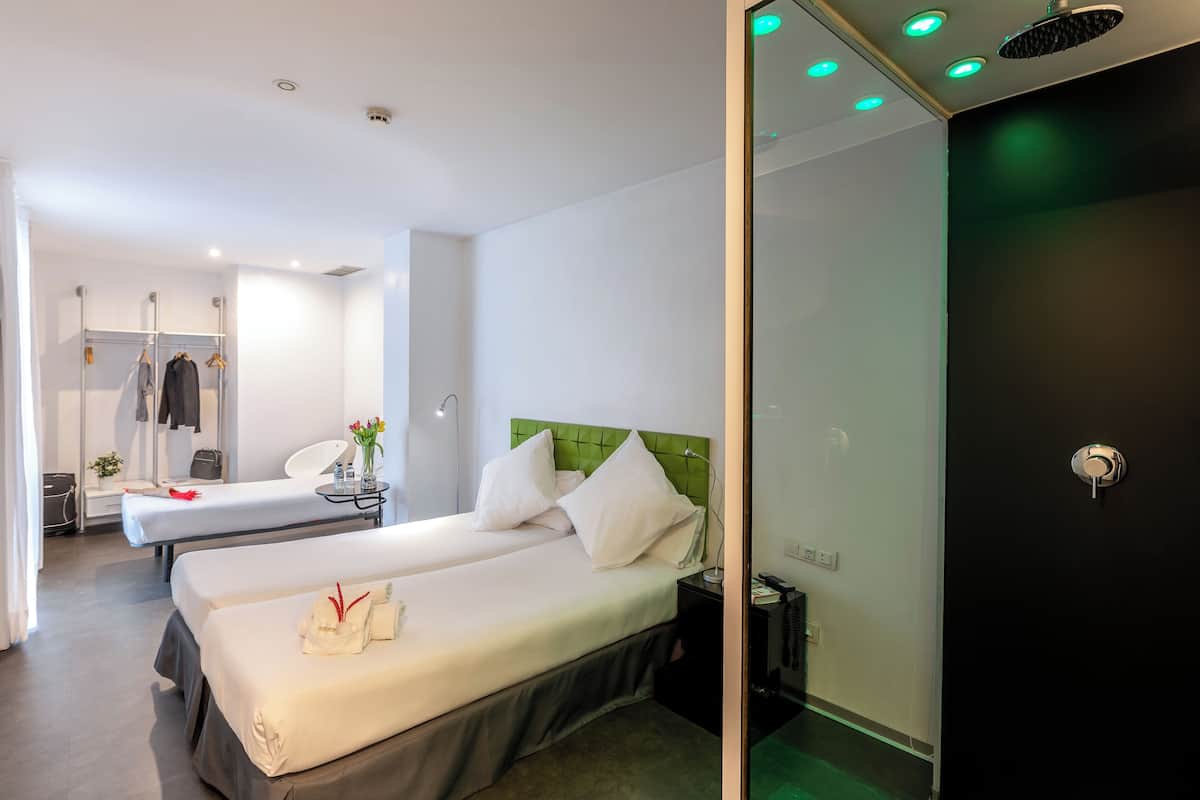 A hotel room with two beds, a mirror, a bedside table with a lamp, and a wardrobe.
