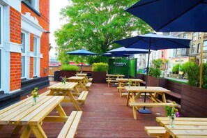 An outdoor patio with wooden tables and benches, covered by blue umbrellas, and a sign for 'Ravado's' in the background. - Revado Hotel, Norwich City Centre (Norwich)