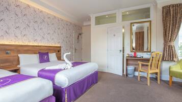Quarto de hotel com duas camas, uma escrivaninha, uma cadeira, um espelho e uma janela com cortinas.