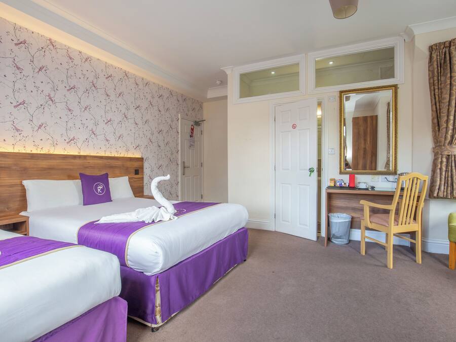 Quarto de hotel com duas camas, uma escrivaninha, uma cadeira, um espelho e uma janela com cortinas.