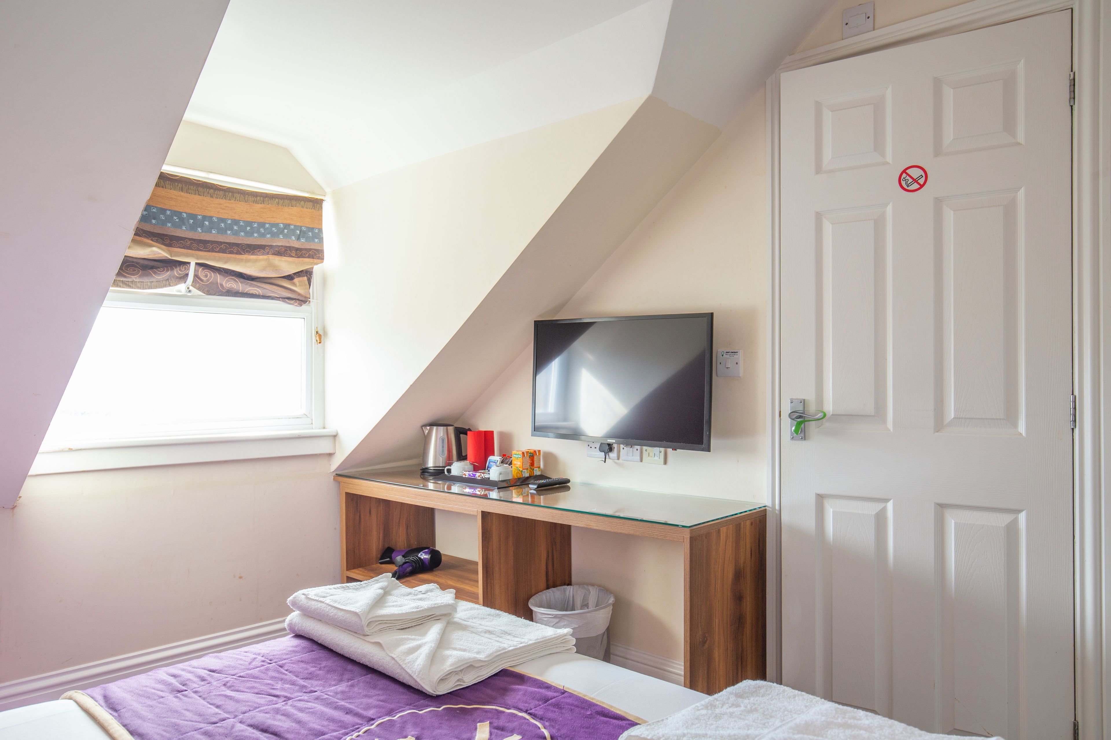 Una habitación con cama, escritorio con televisor de pantalla plana, ventana con cortinas y puerta con letrero de 'no fumar'.