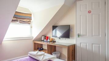 Una habitación con cama, escritorio con televisor de pantalla plana, ventana con cortinas y puerta con letrero de 'no fumar'.