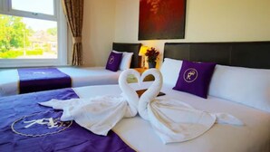 A hotel room with two beds, each with a purple headboard and pillow, and a large window with curtains. - Revado Hotel, Norwich City Centre (Norwich)
