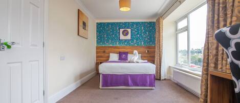 Habitación de hotel con cama, ventana, puerta y pared con estampado floral.