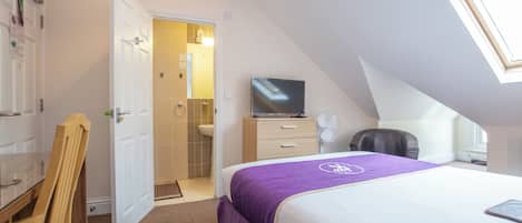 Un dormitorio con una cama, televisión, escritorio y una silla.