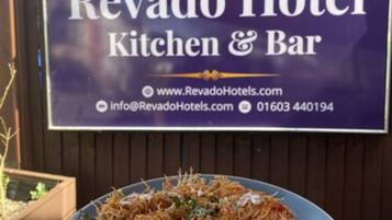 A sign for Revado Hotel Kitchen & Bar with contact information and a plate of food.