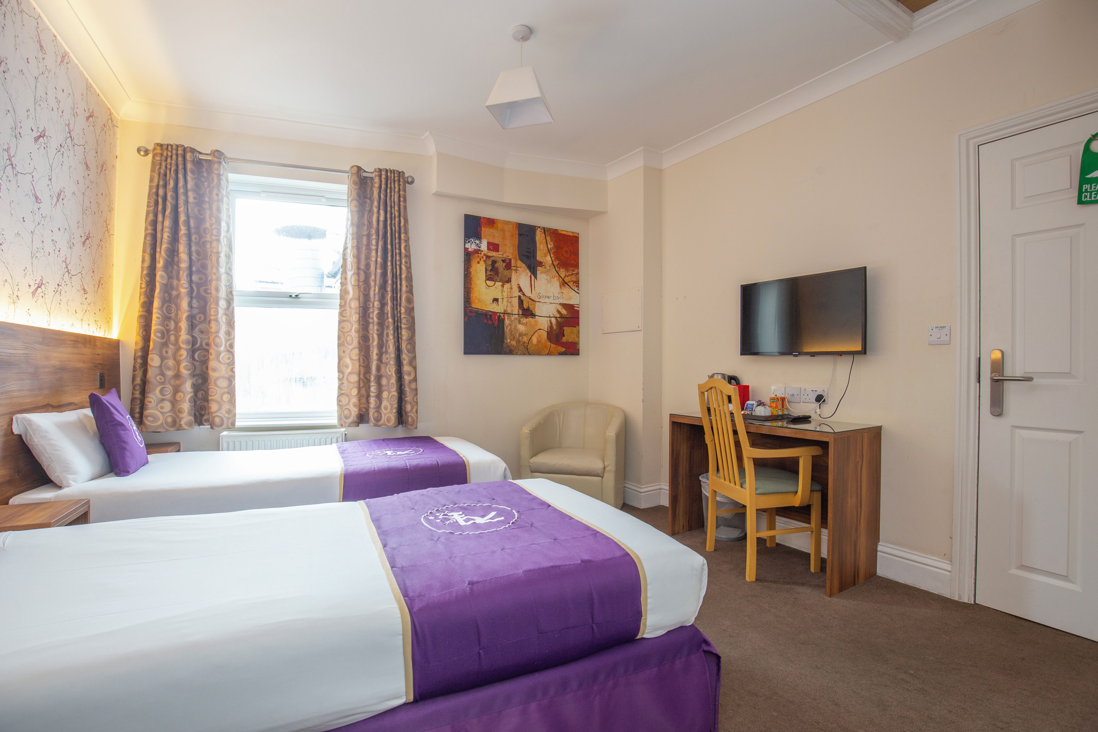 A hotel room with two beds, a desk, a chair, a television, and a painting on the wall.