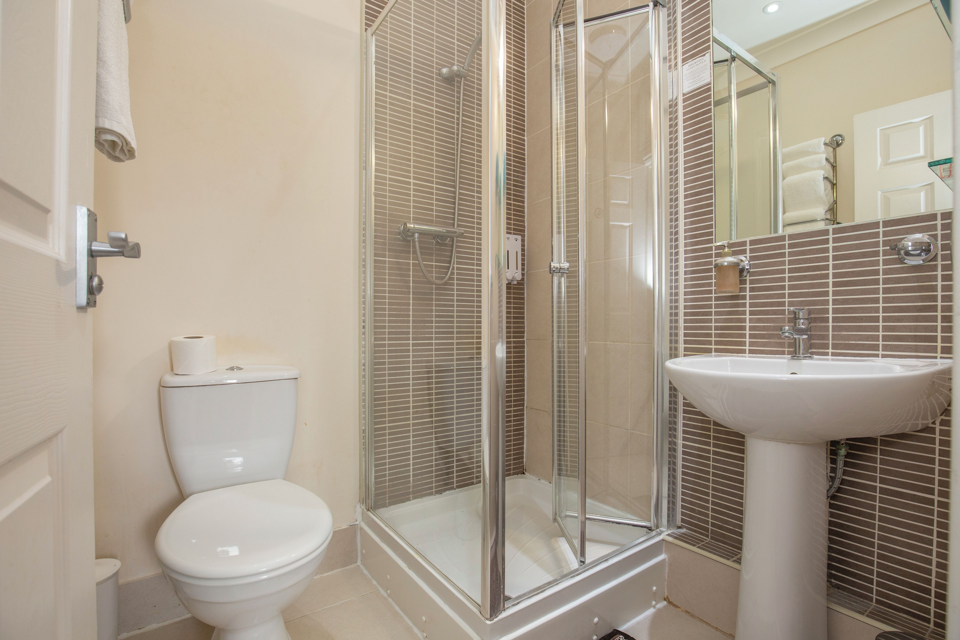 A bathroom with a toilet, a glass-enclosed shower, and a pedestal sink.