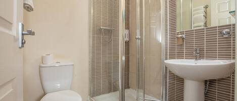 A bathroom with a toilet, a glass-enclosed shower, and a pedestal sink.