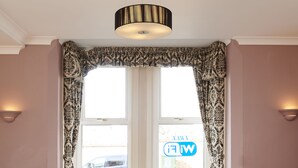 A dining area with a table and four chairs, a window with patterned curtains, and a hanging light fixture. - Revado Hotel, Norwich City Centre (Norwich)