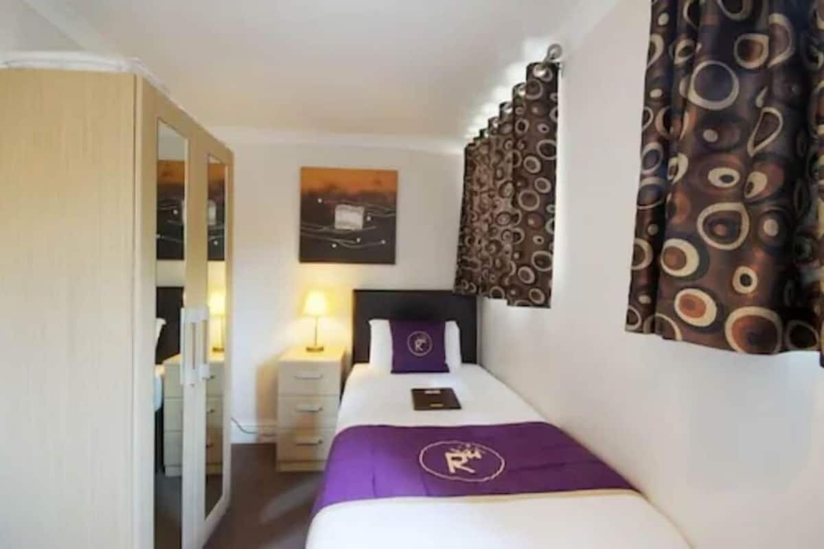 A hotel room with a bed, a nightstand, a mirror, a wardrobe, and a painting on the wall.