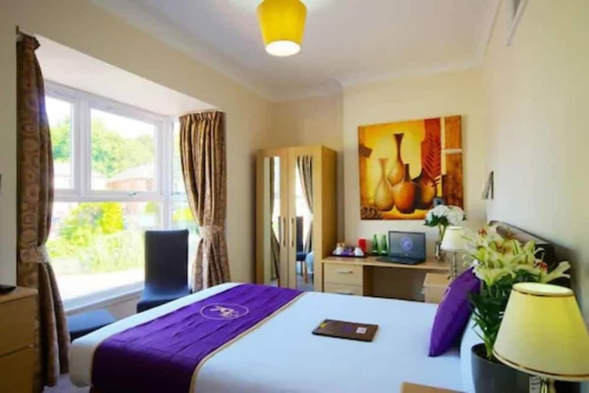 A hotel room with a bed, a desk, a chair, a wardrobe, and a painting on the wall.