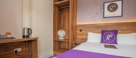 Habitación de hotel con cama, escritorio de madera, tetera, ventilador y una pared con un logotipo.