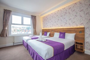 A hotel room with two beds, a large window, and a floral wallpaper.