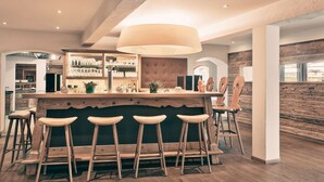 A bar area with wooden stools, a large hanging light fixture, and a display of bottles and glasses. - POP-UP LIVING Zell am See (Zell am See)