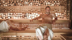 A man sitting on a wooden bench with a backdrop of stacked logs. - POP-UP LIVING Zell am See (Zell am See)