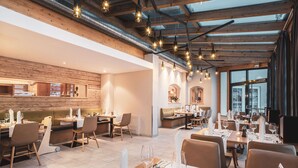 A modern restaurant with exposed wooden beams, hanging pendant lights, and a mix of dining areas. - POP-UP LIVING Zell am See (Zell am See)