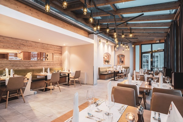 A modern restaurant with exposed wooden beams, hanging pendant lights, and a mix of dining areas.