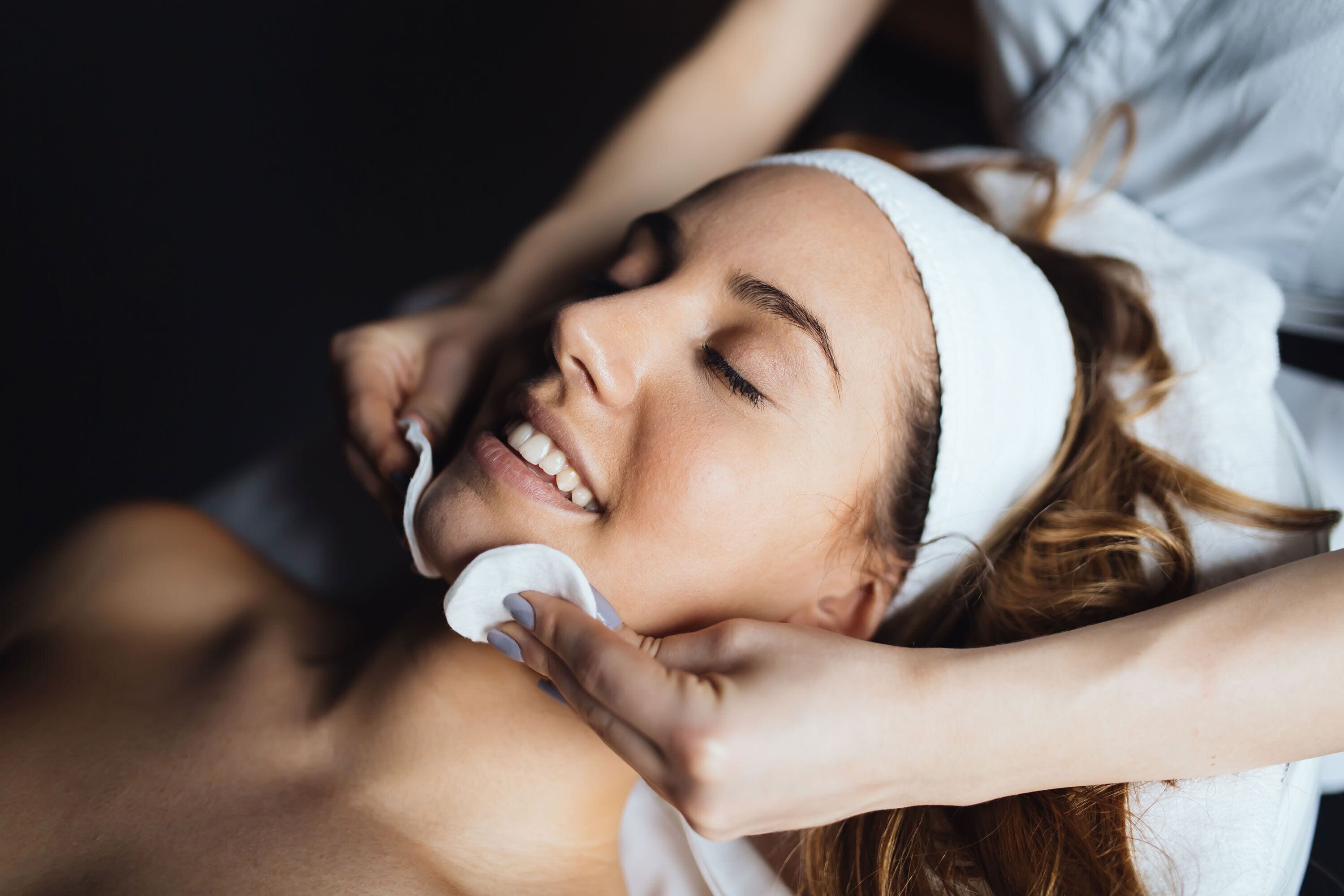 A person lying down with a white headband, receiving a facial treatment.