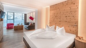 A modern hotel room with a wooden accent wall, a bed with white linens, a small side table, a red lamp, and a view of the outdoors through large windows. - POP-UP LIVING Zell am See (Zell am See)