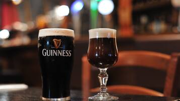 Two glasses of beer, one with a Guinness logo and the other empty, on a bar counter.