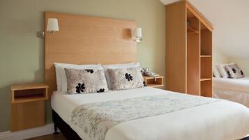 A neatly arranged hotel room with a large bed, a wooden wardrobe, a bedside table with a lamp, and a telephone.