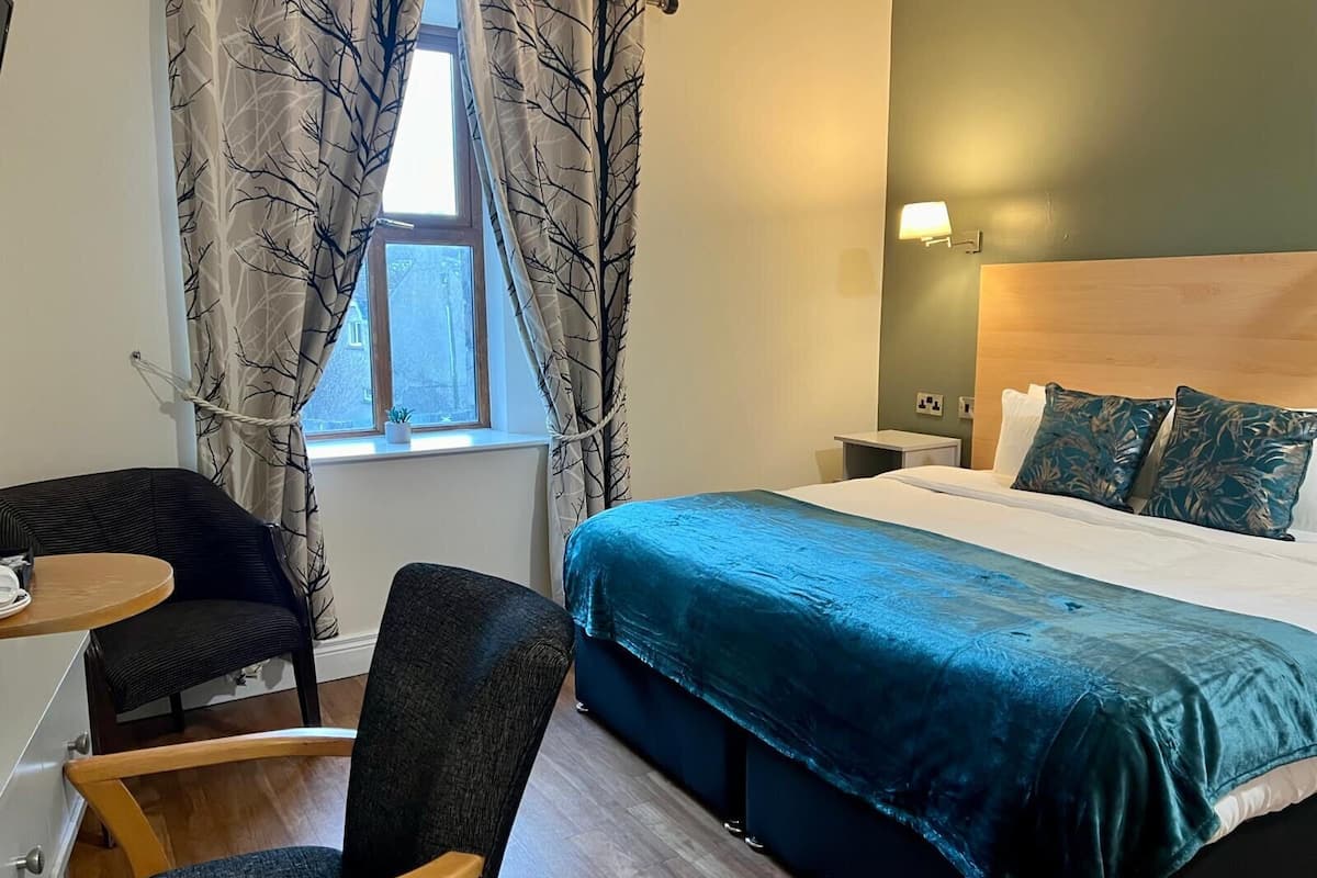 Ett hotellrum med en säng, ett skrivbord, en stol, ett nattduksbord och ett fönster med gardiner.