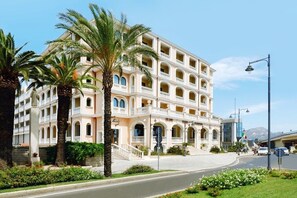 Un hotel de varios pisos con un patio central, palmeras y un cielo azul despejado.
