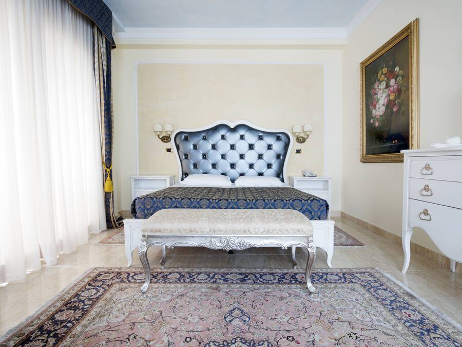 A bedroom with a large bed, a bench, a nightstand, a dresser, and a painting on the wall.