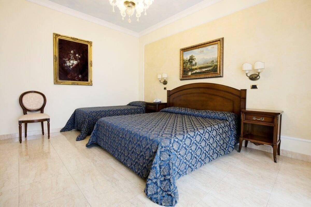 Une chambre avec deux lits, une table de chevet en bois, une chaise et deux lampes fixées au mur.